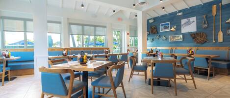 A restaurant interior with high ceilings, natural light from large windows, and a variety of seating arrangements including tables and booths.