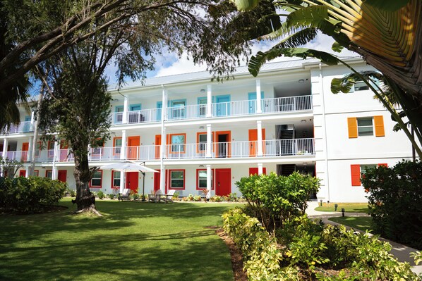 A multi-story hotel with balconies, a well-maintained lawn, and a variety of plants.
