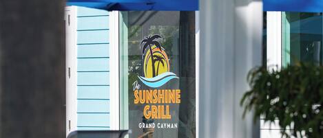 Letrero de restaurante con logotipo de palmera y el nombre 'Sunshine Grill' en un edificio.