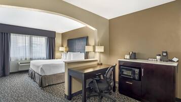 A hotel room with a bed, desk, chair, microwave, and a minibar.