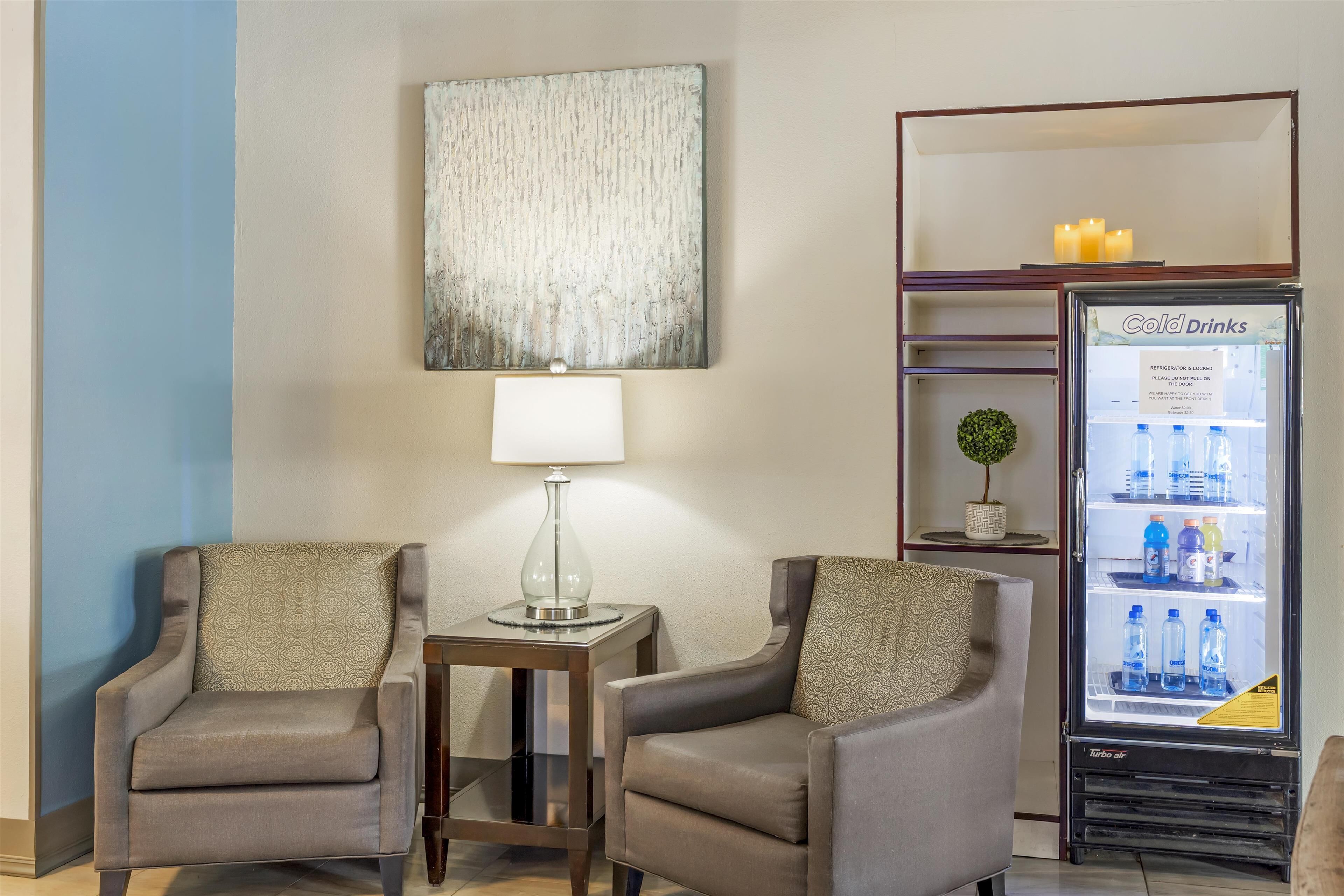 Een hotelkamer met twee fauteuils, een bijzettafeltje met een lamp, een kunstwerk aan de muur en een minibar gevuld met drankjes.