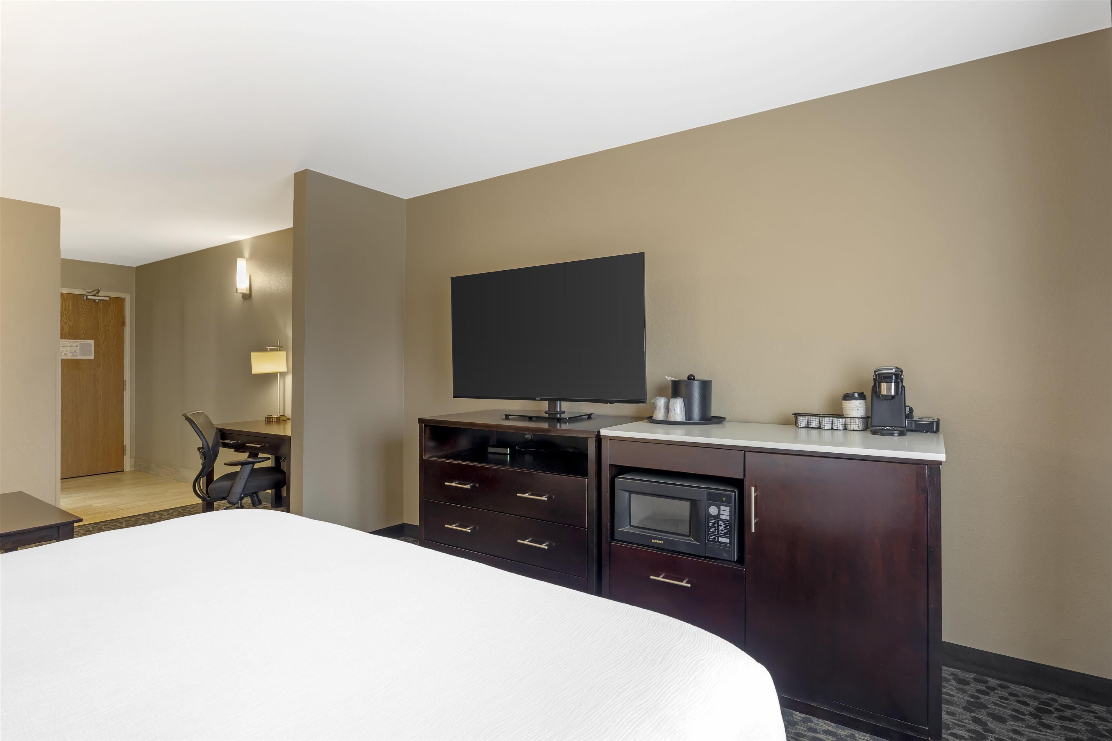 Habitación de hotel con cama, escritorio con silla, televisión, microondas y cafetera.