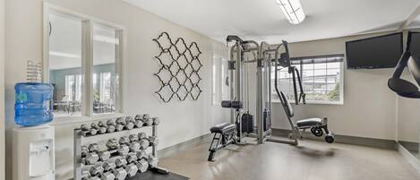 Un gimnasio limpio y bien iluminado con equipo de ejercicio, un dispensador de agua y un estante con mancuernas.