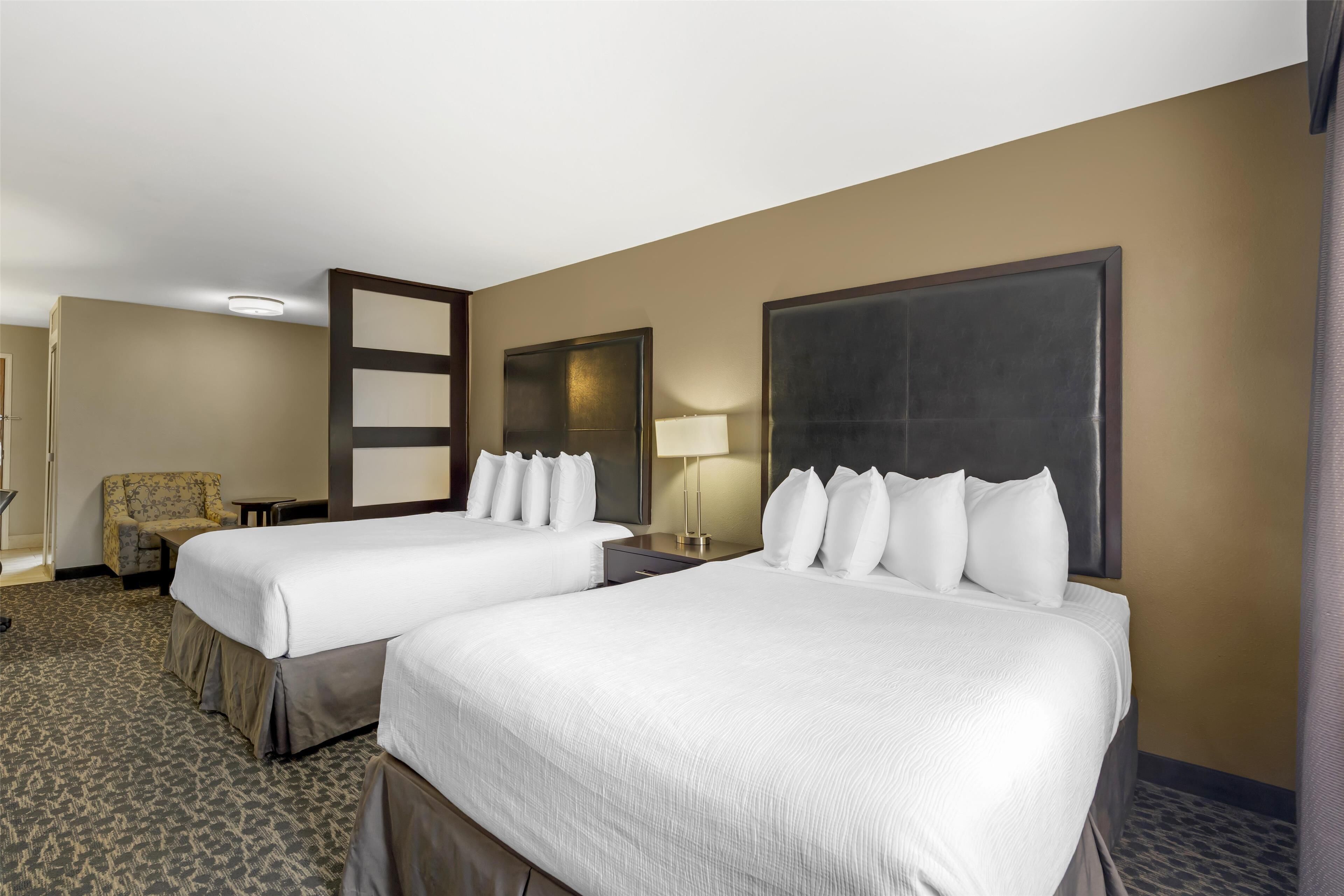 Une chambre d’hôtel avec deux lits, une chaise, un bureau et une lampe.