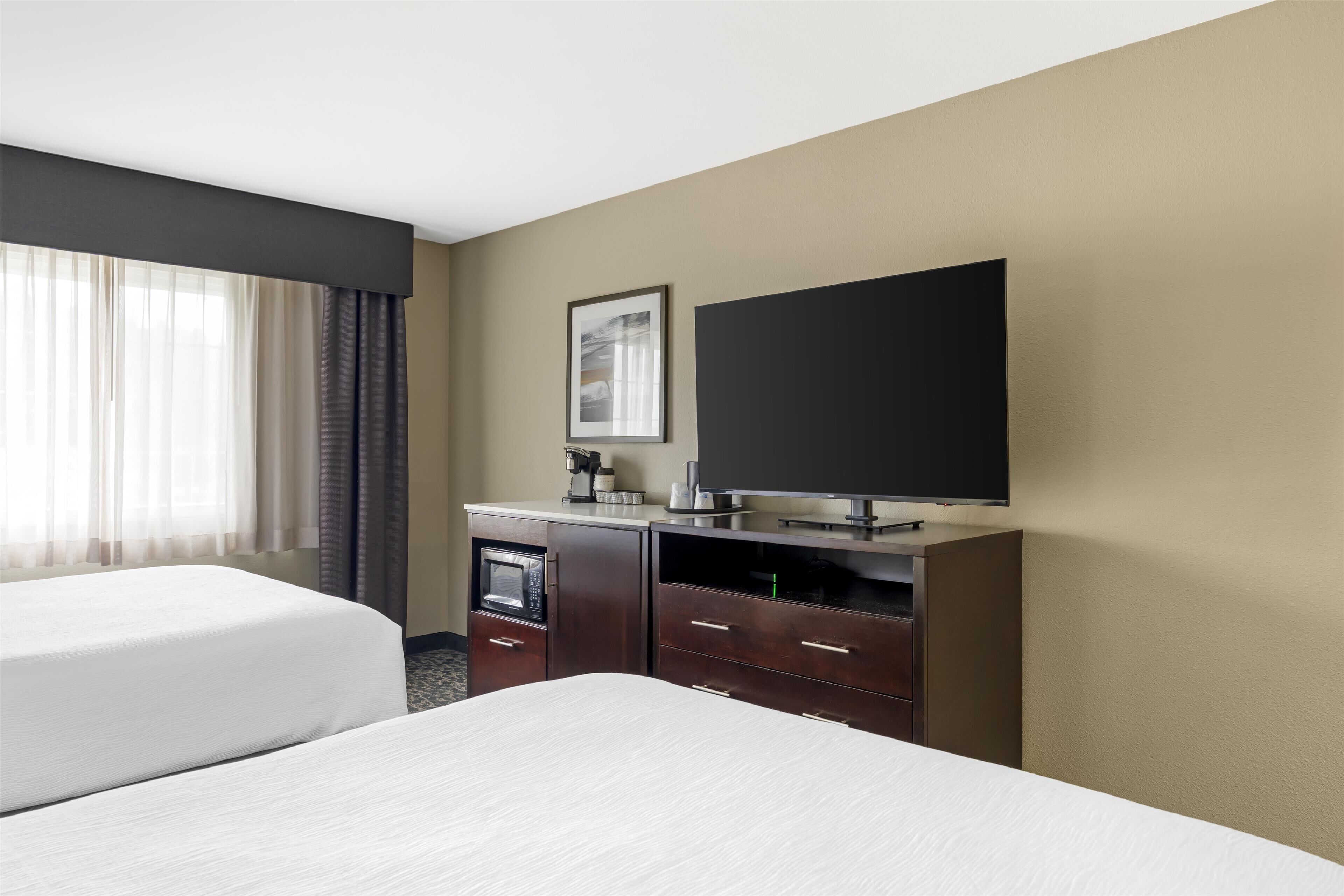A hotel room with a bed, a flat-screen TV, a minibar, and a window with curtains.