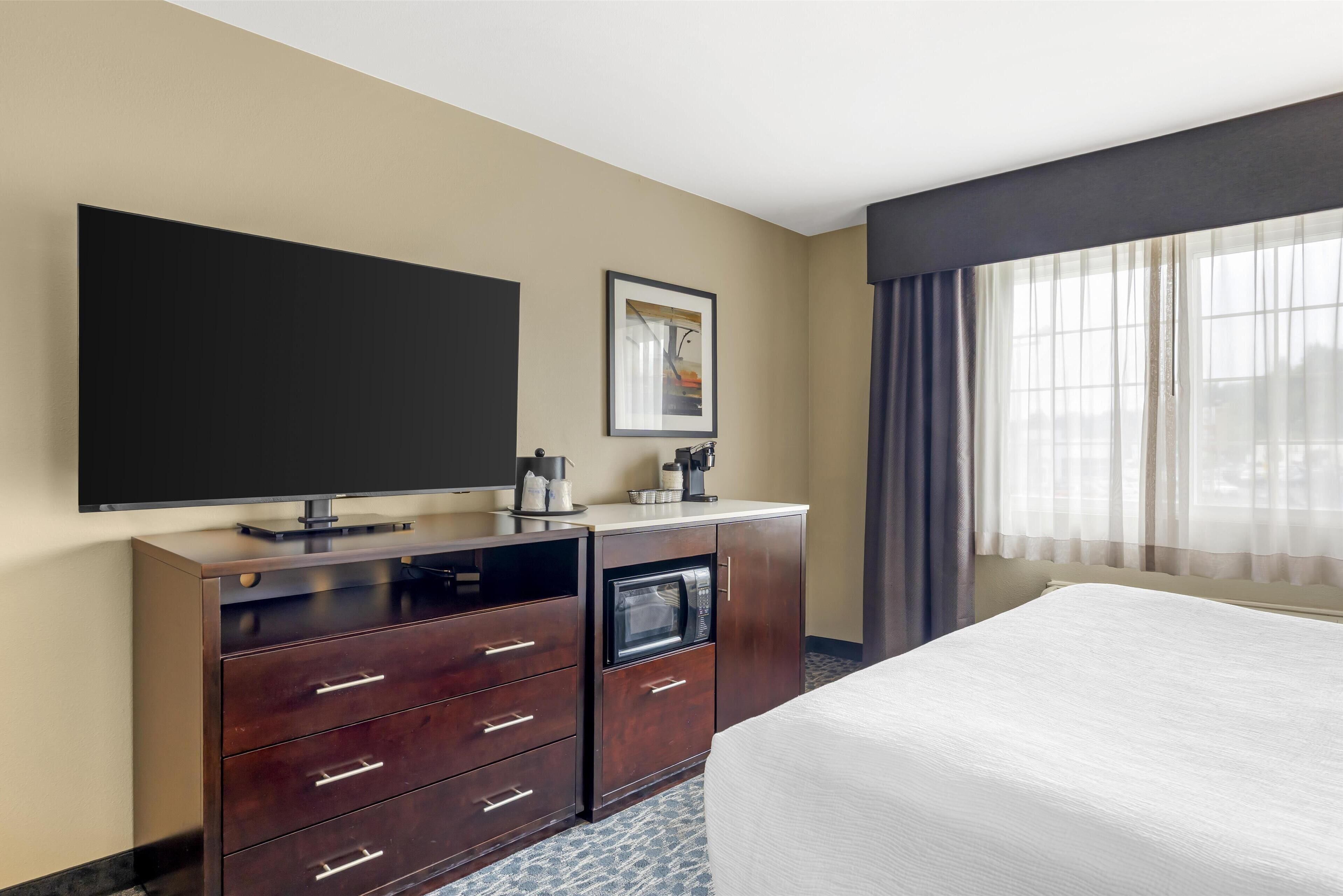 Een hotelkamer met een bed, een flatscreen televisie, een minibar, een magnetron en een ingelijst schilderij aan de muur.