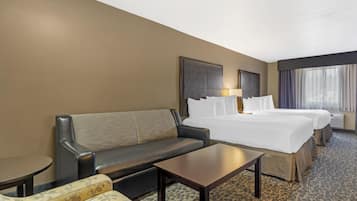 A hotel room with a sofa, two beds, a small table, and a window with curtains.