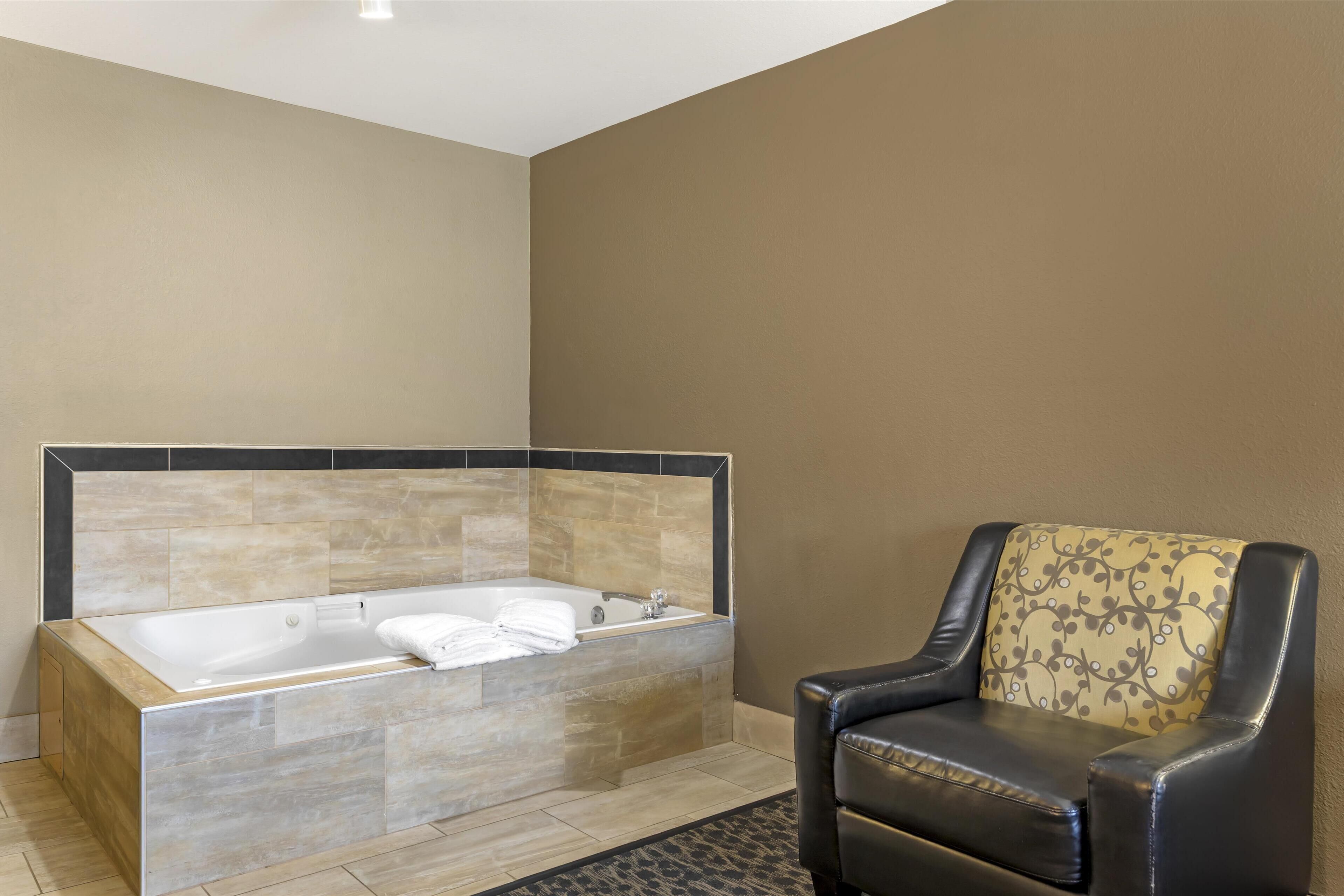 A modern bathroom with a large bathtub, a black leather chair, and a patterned cushion.