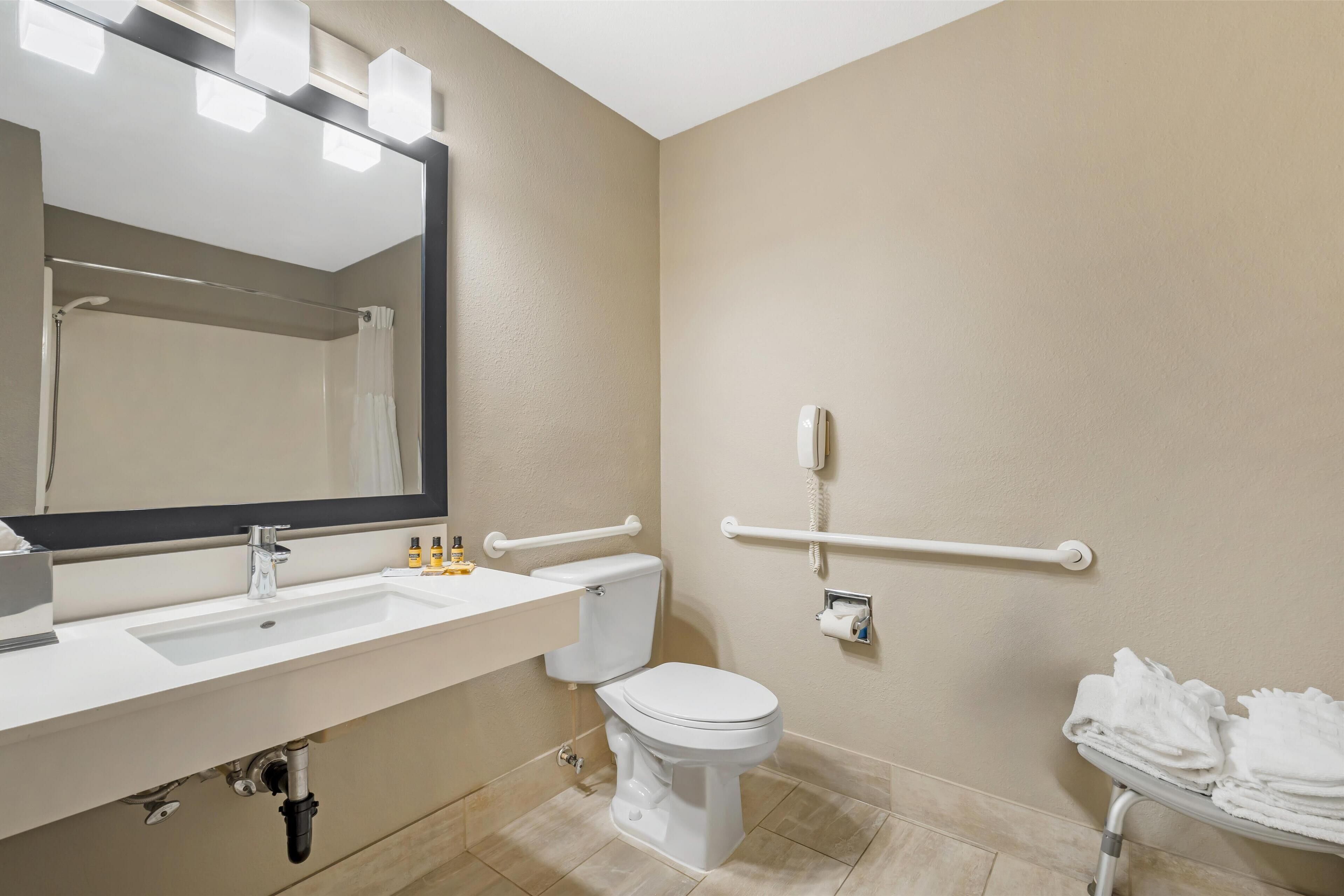A bathroom with a sink, mirror, toilet, and a handrail.