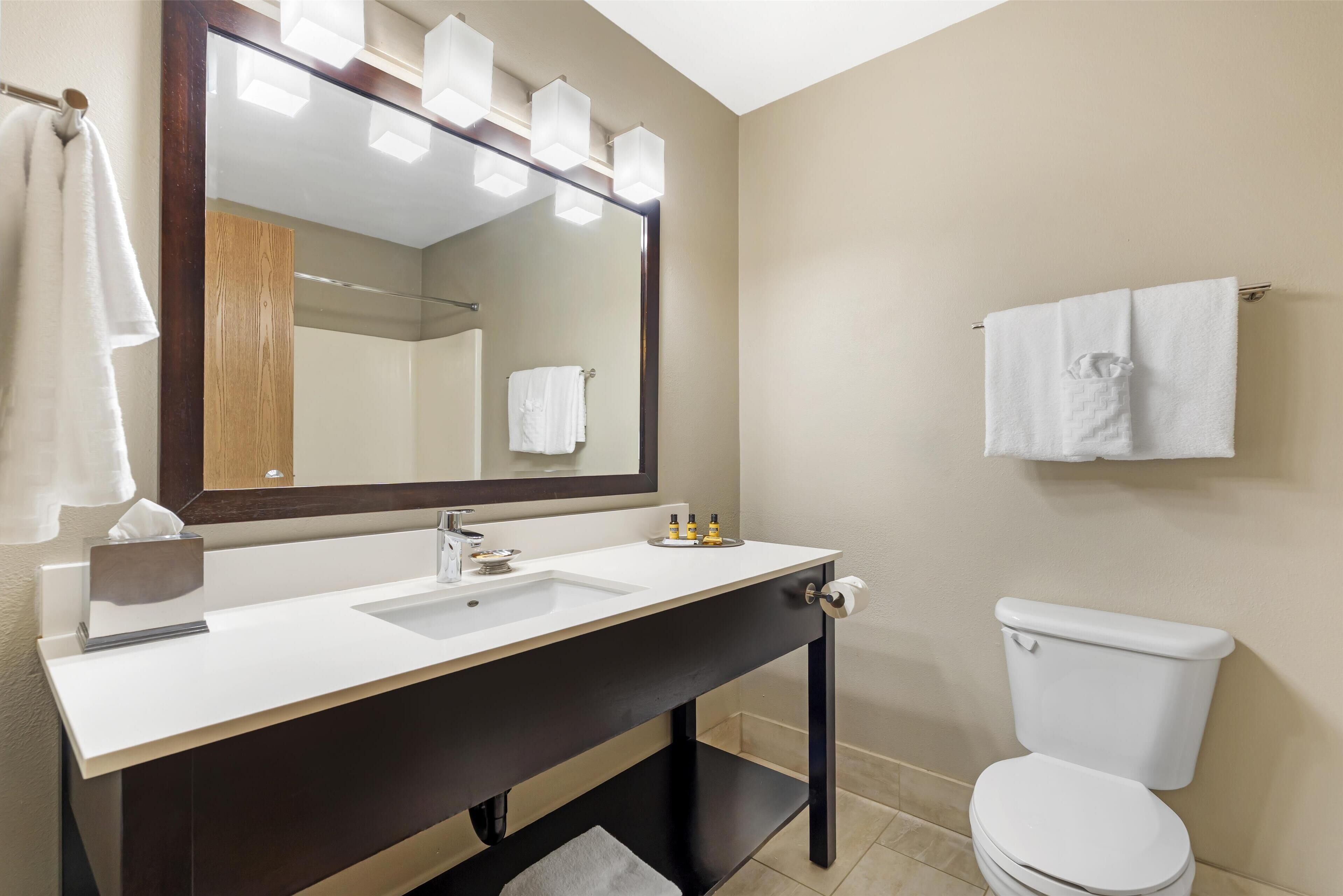 A modern bathroom with a large mirror, white sink, dark vanity, and a white toilet.
