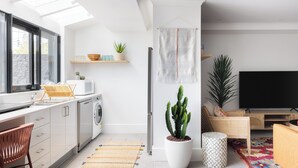 A modern kitchen with a washing machine, a dining area with a TV, and a living room with a couch and a plant. - Hotel Hacienda (Redfern)