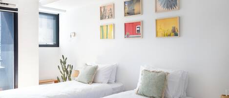 A hotel room with two beds, a window, and four framed artworks on the wall.