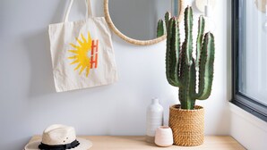 A room with a wooden dresser, a mirror, a cactus, a hat, and a tote bag. - Hotel Hacienda (Redfern)