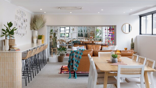 A spacious dining area with a long table and multiple chairs, a bar with stools, and a variety of plants and decorative items. - Hotel Hacienda (Redfern)