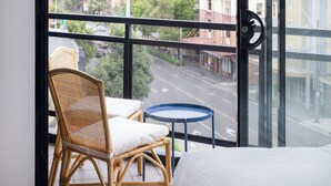 A balcony with wicker chairs and a small table, overlooking a street with buildings and trees. - Hotel Hacienda (Redfern)