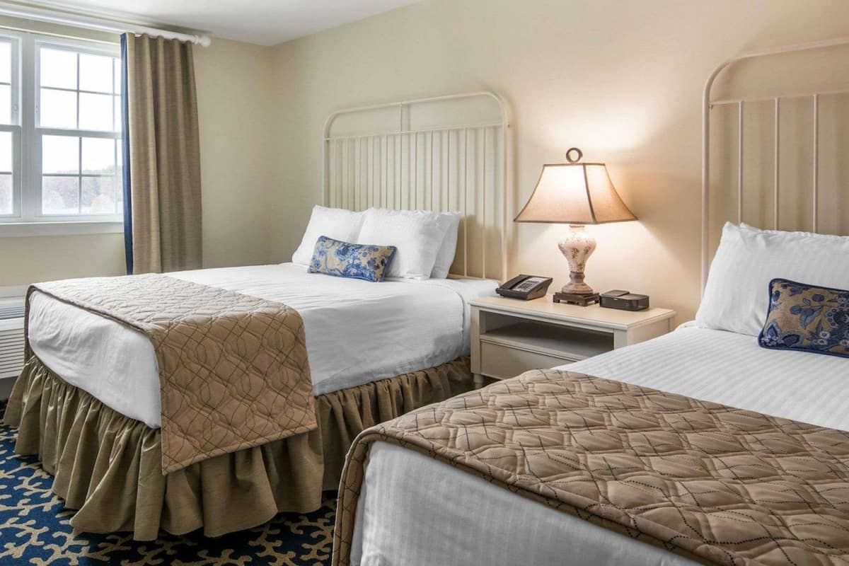 Une chambre d’hôtel avec deux lits, une table de chevet avec une lampe, un téléphone et une fenêtre avec des rideaux.