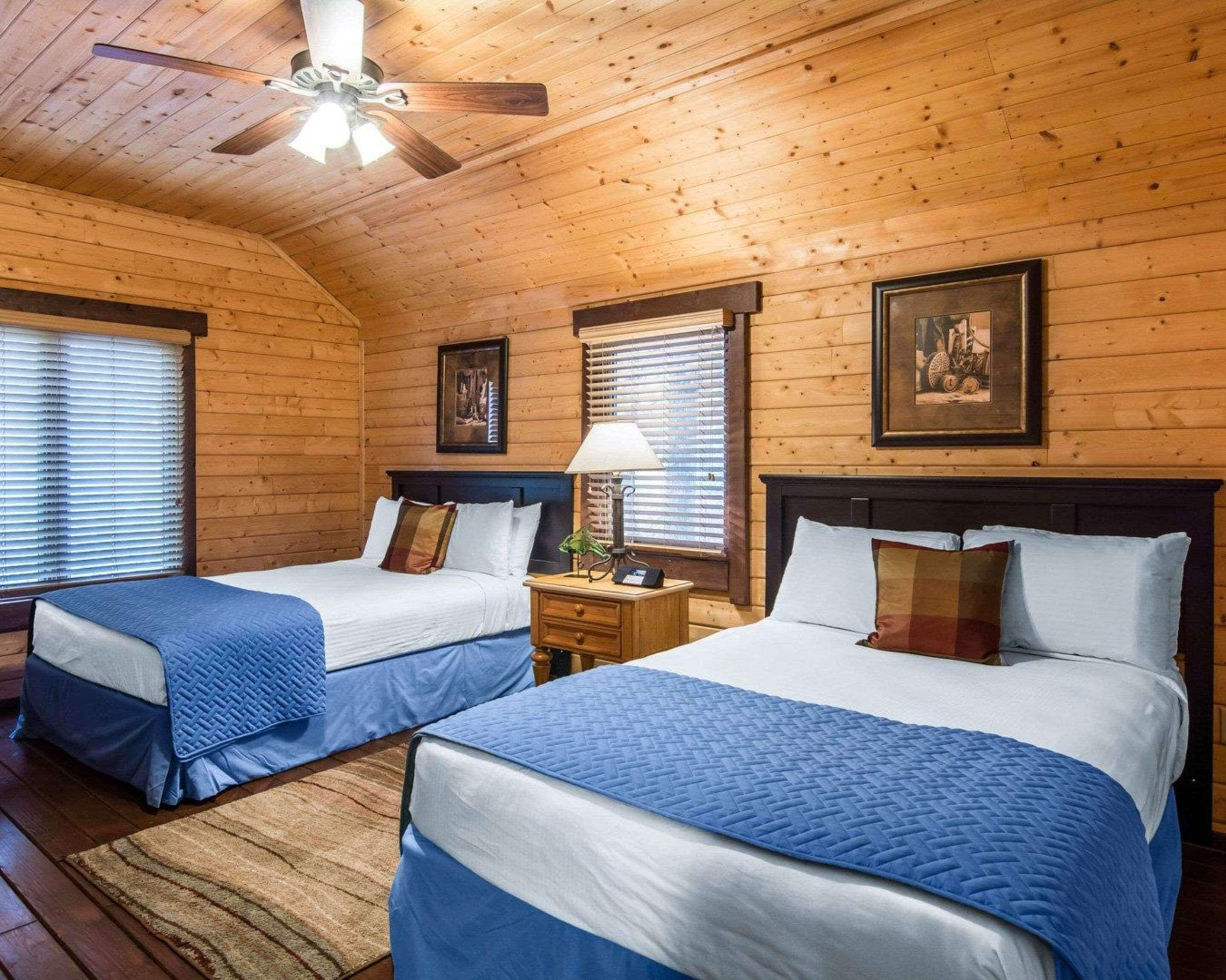 Ein Zimmer in einer Holzhütte mit zwei Betten, einem Deckenventilator und einem gerahmten Bild an der Wand.