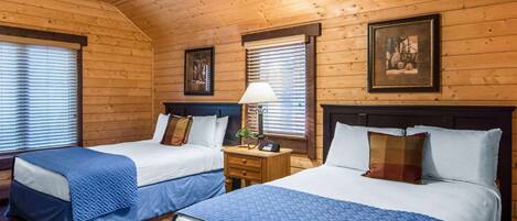 Ein Zimmer in einer Holzhütte mit zwei Betten, einem Deckenventilator und einem gerahmten Bild an der Wand.
