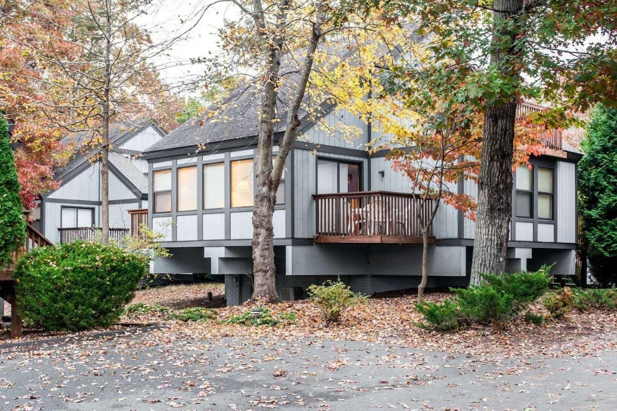 Une maison moderne à deux étages, dotée d’un balcon et entourée d’arbres aux feuilles d’automne.
