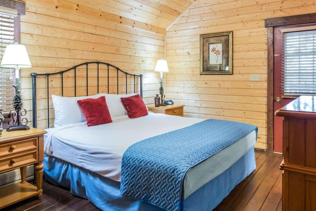 Une chambre à coucher aux murs lambrissés, avec un lit, deux tables de chevet, des lampes et un tableau encadré accroché au mur.