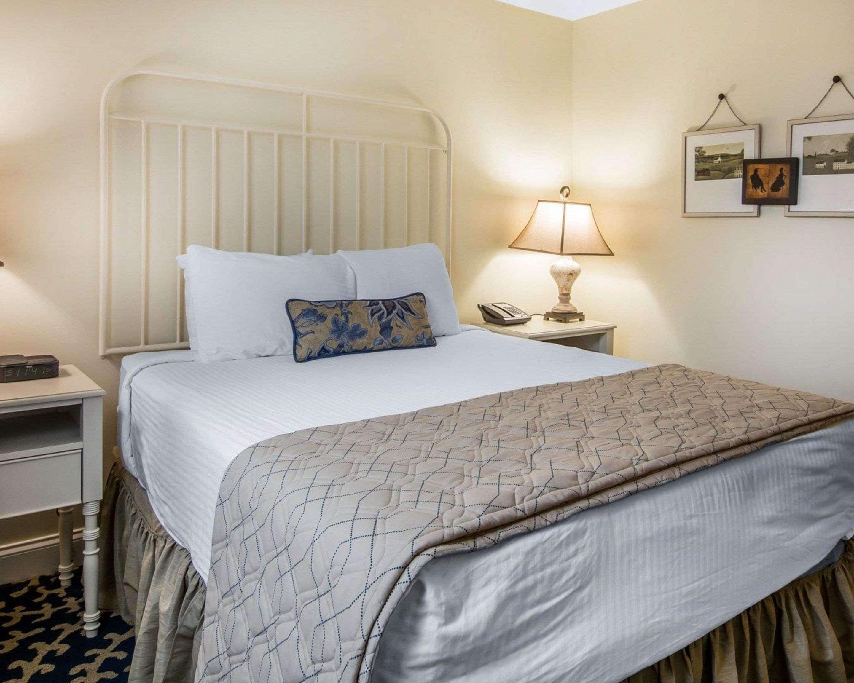 A neatly made bed with a patterned bedspread, a bedside lamp, and a nightstand with a phone.