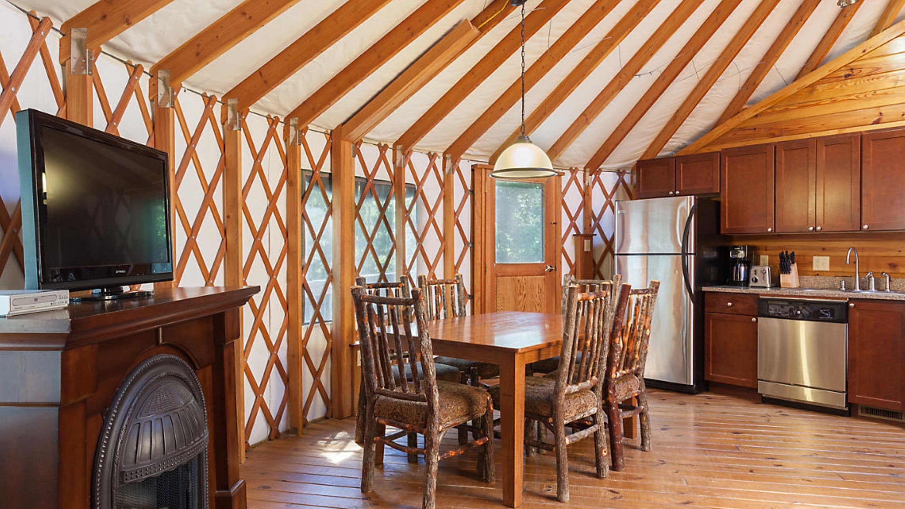 A rustic kitchen with wooden beams, a dining table with chairs, a TV, and a refrigerator.