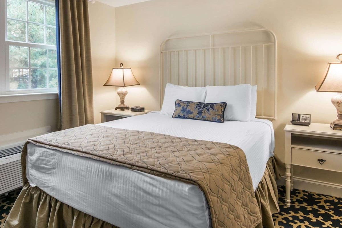 Une chambre d’hôtel avec un lit, deux tables de chevet, une fenêtre avec des rideaux et un radiateur.