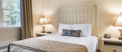 A hotel room with a bed, two bedside tables, a window with curtains, and a radiator.