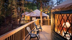 Une terrasse en bois avec des chaises, un espace abrité et une structure ressemblant à une tente, le tout situé dans un cadre boisé.