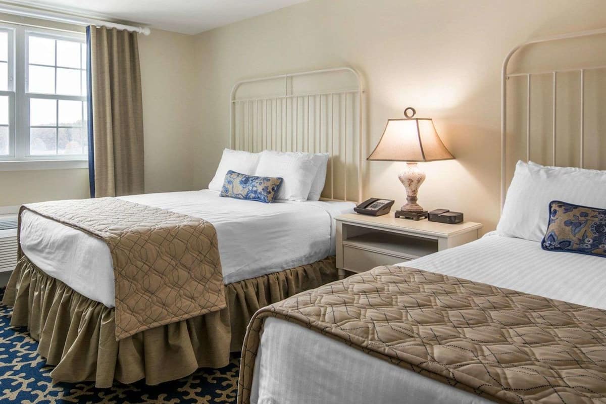 Une chambre d’hôtel avec deux lits, une table de chevet avec une lampe, un téléphone et une fenêtre avec des rideaux.