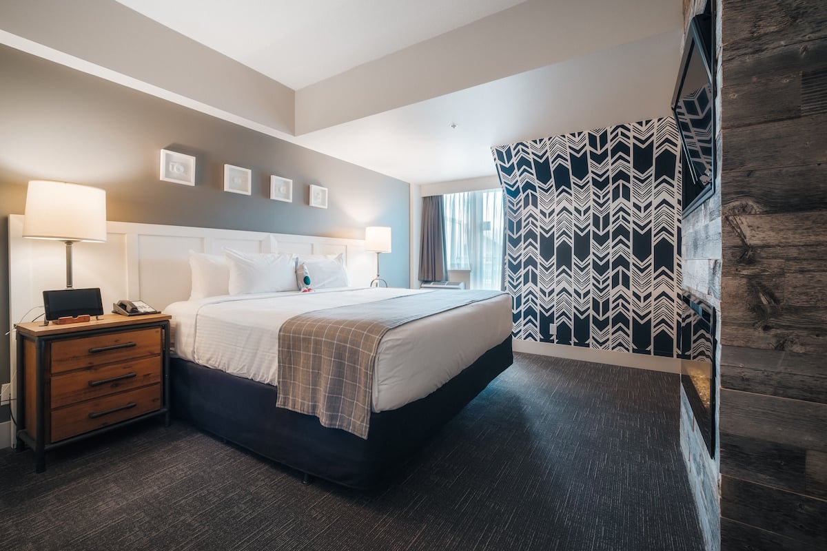 Een hotelkamer met een groot bed, een houten nachtkastje, een bureau met een lamp en een gordijn met een patroon.