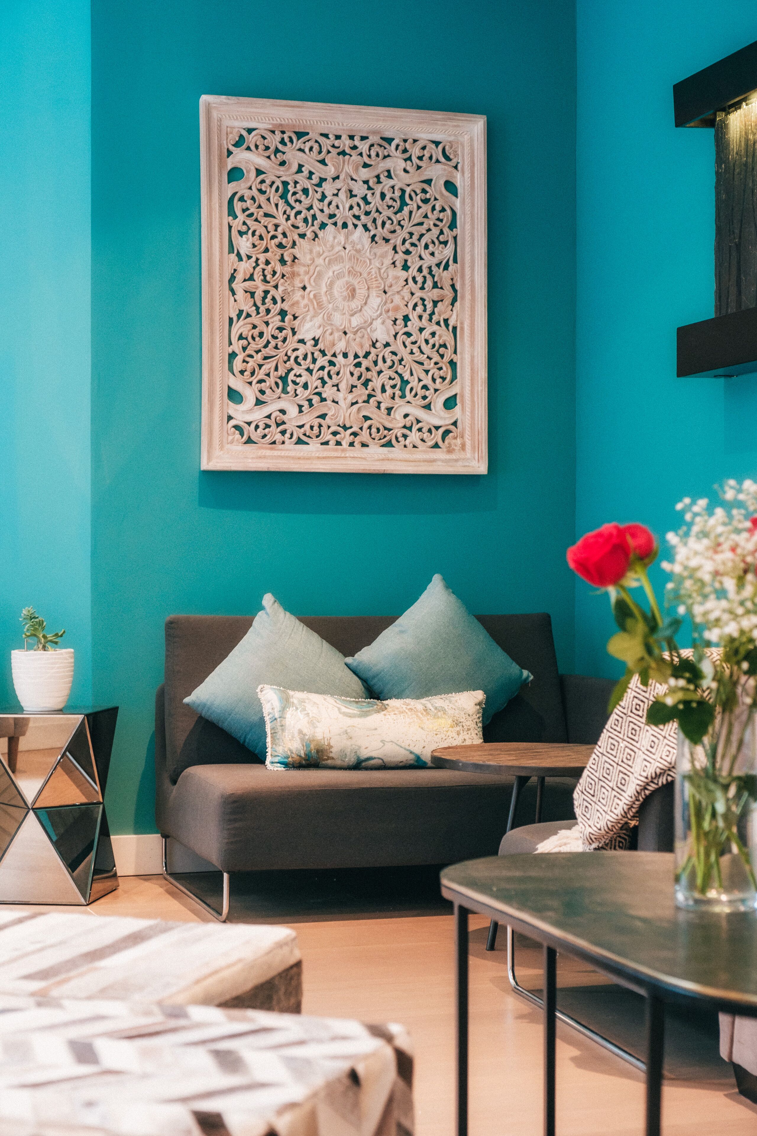 A teal-colored room with a sofa, pillows, a table, and a decorative wall piece.