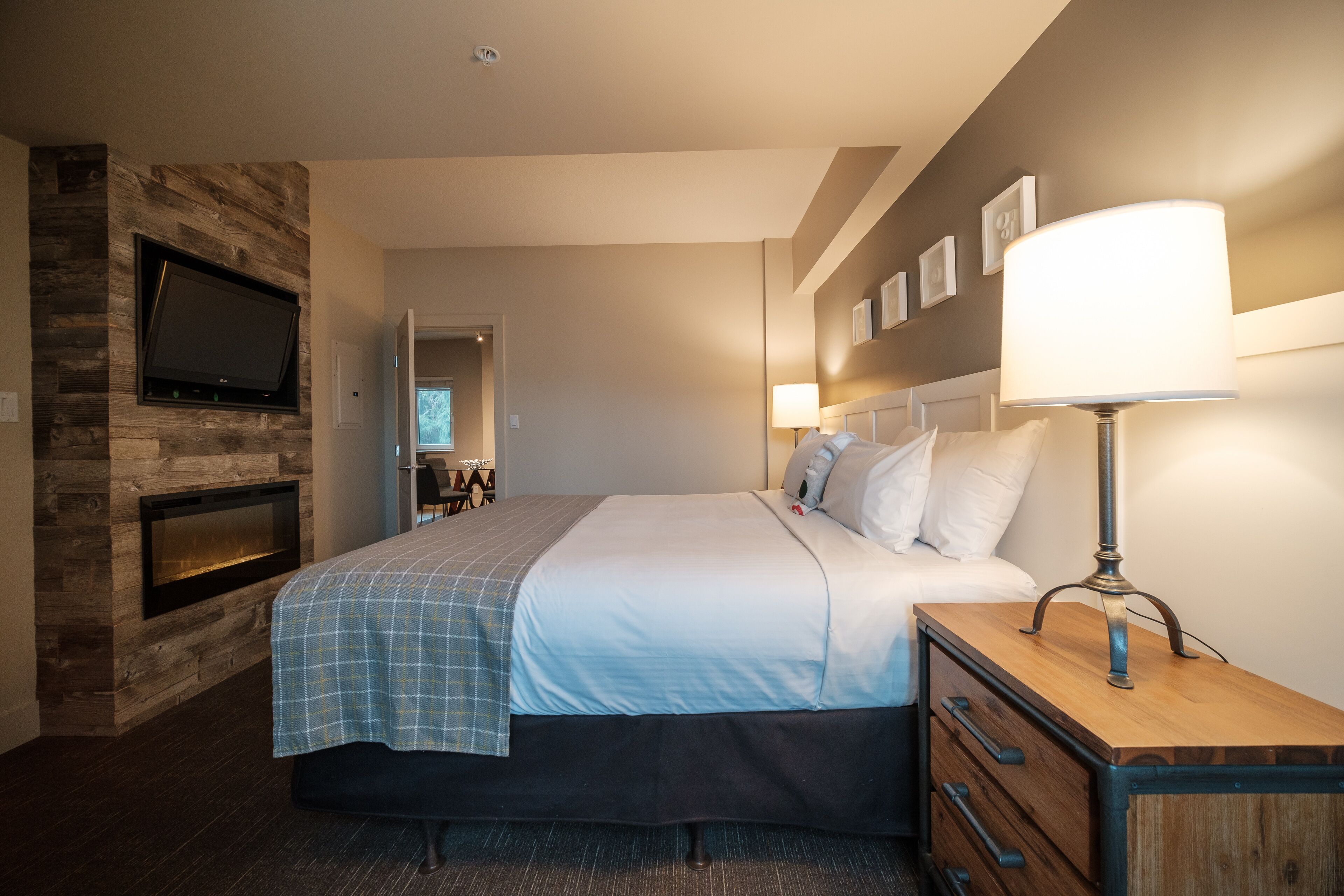 Une chambre d’hôtel avec un lit, une table de chevet, une lampe, un téléviseur fixé à un mur en bois et une cheminée.