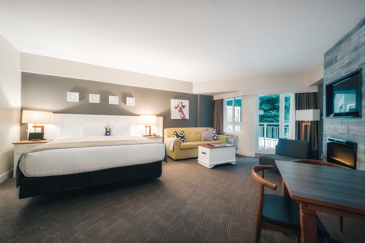 Een moderne hotelkamer met een groot bed, een sofa, een eettafel en een televisie.