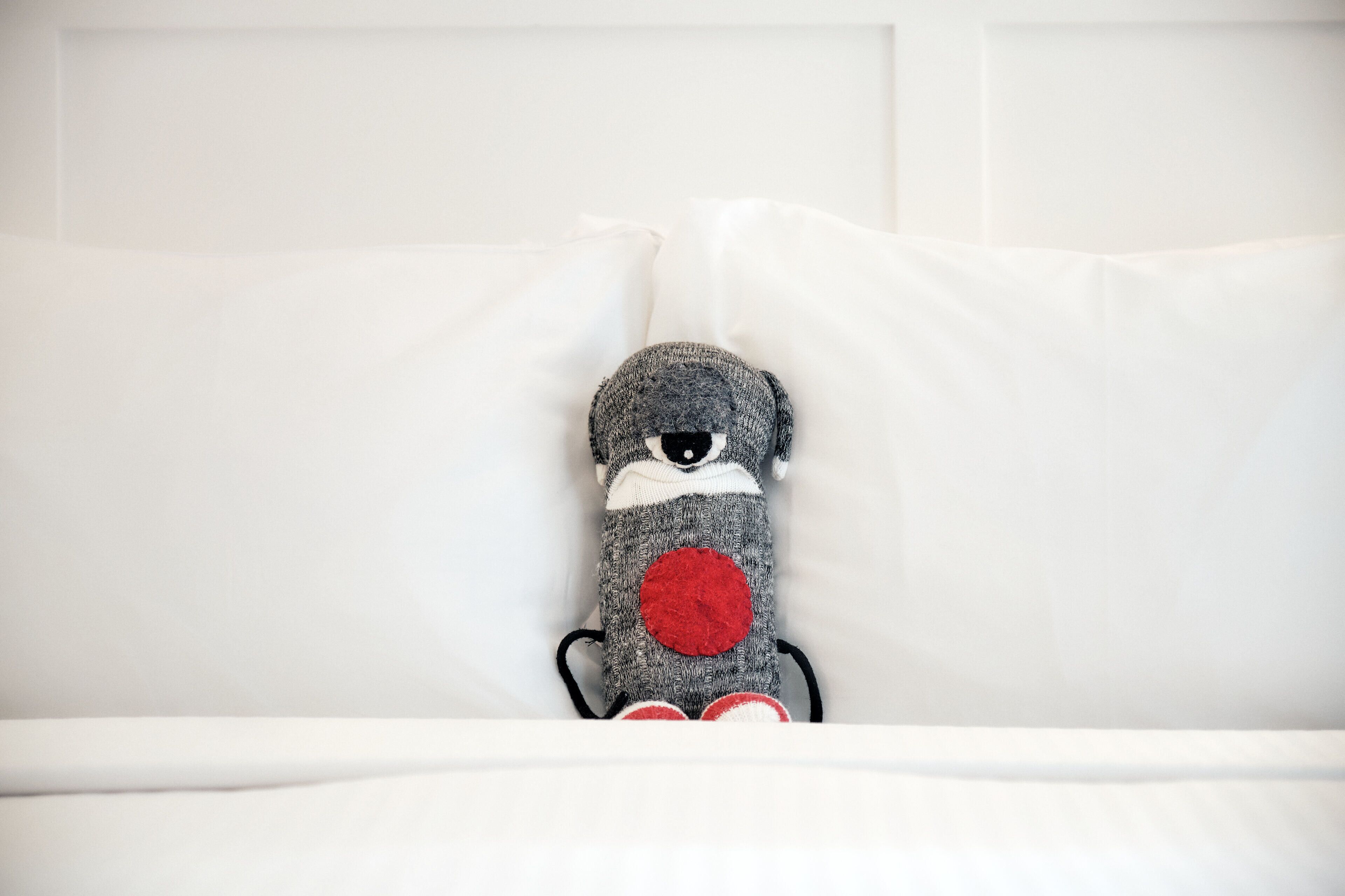 Un peluche sobre una cama blanca con almohadas.