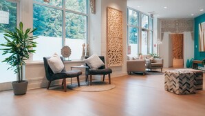 Un salón espacioso con amplias ventanas, una planta en maceta, dos sillones, una mesa de centro y un panel decorativo.