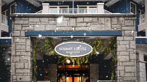 Exterior del Summit Lodge Whistler, con fachada de piedra y un letrero sobre la entrada.
