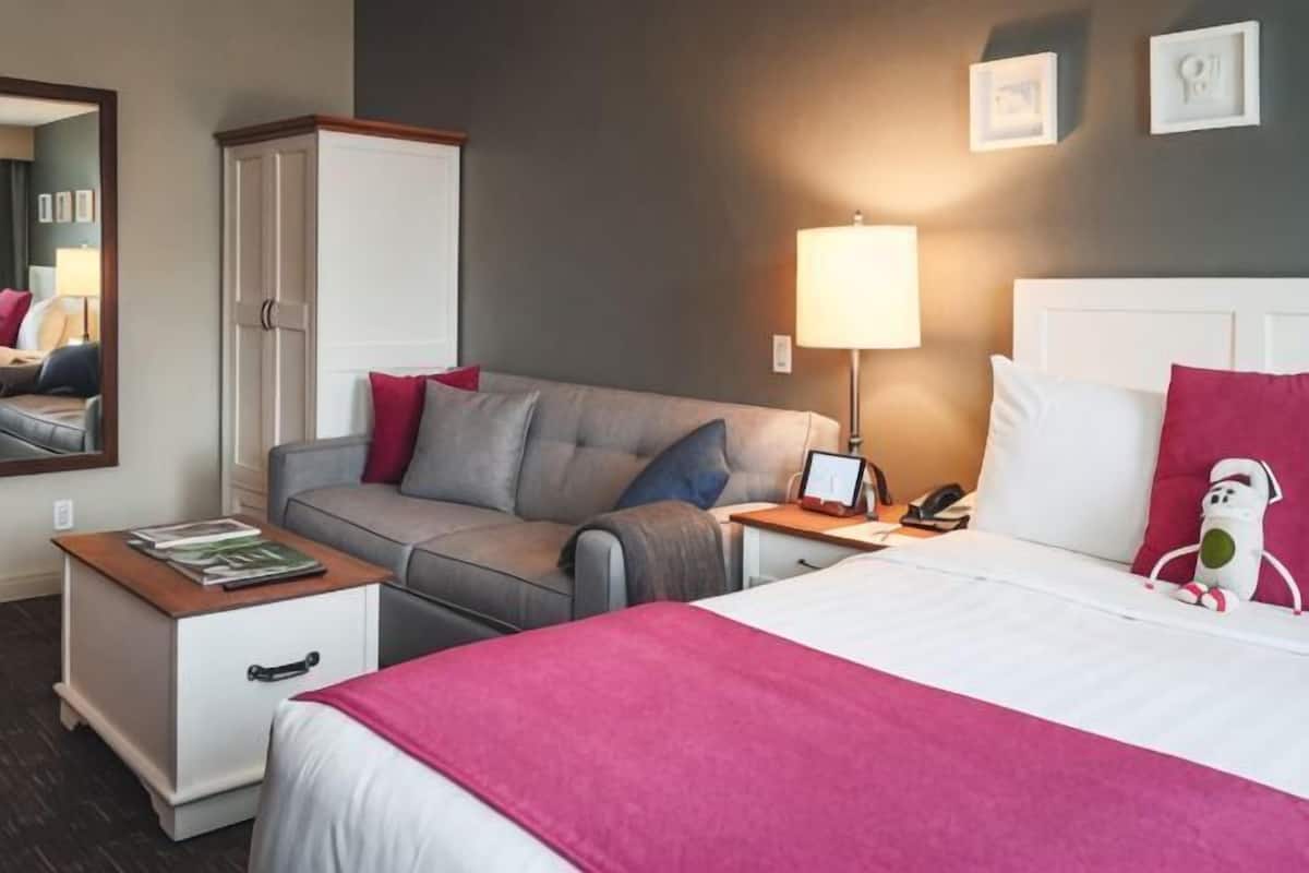 Een hotelkamer met een bed, een slaapbank, een nachtkastje, een lamp, een spiegel en een kledingkast.