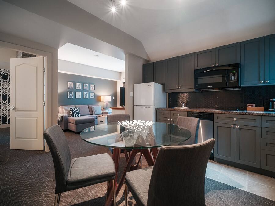A modern kitchen with dark cabinets, a microwave, and a refrigerator. There is a glass dining table with chairs in the foreground.