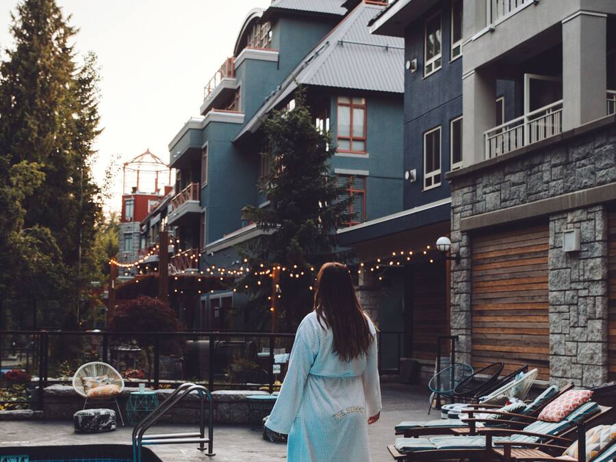 A person walking by a poolside with lounge chairs and a building with balconies.