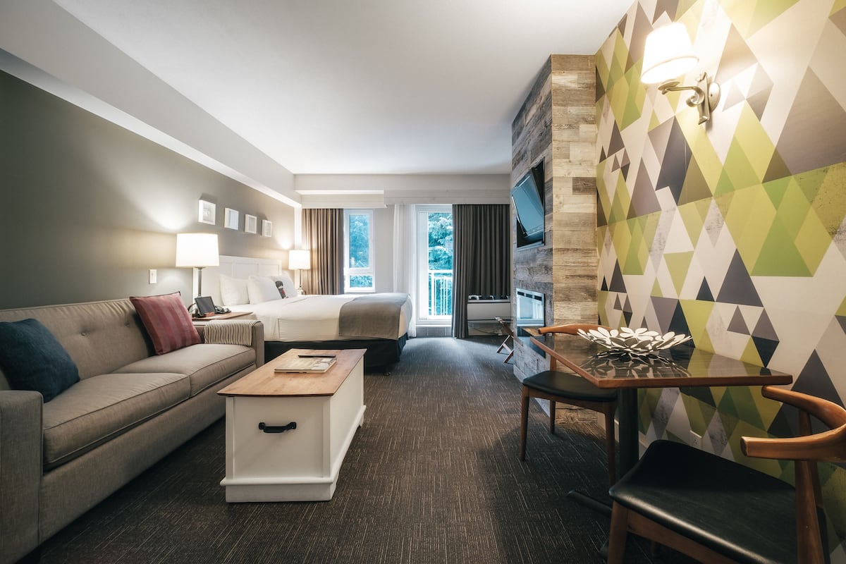 Hotelkamer met een bed, een slaapbank, een salontafel, een televisie en een muur met geometrische patronen.