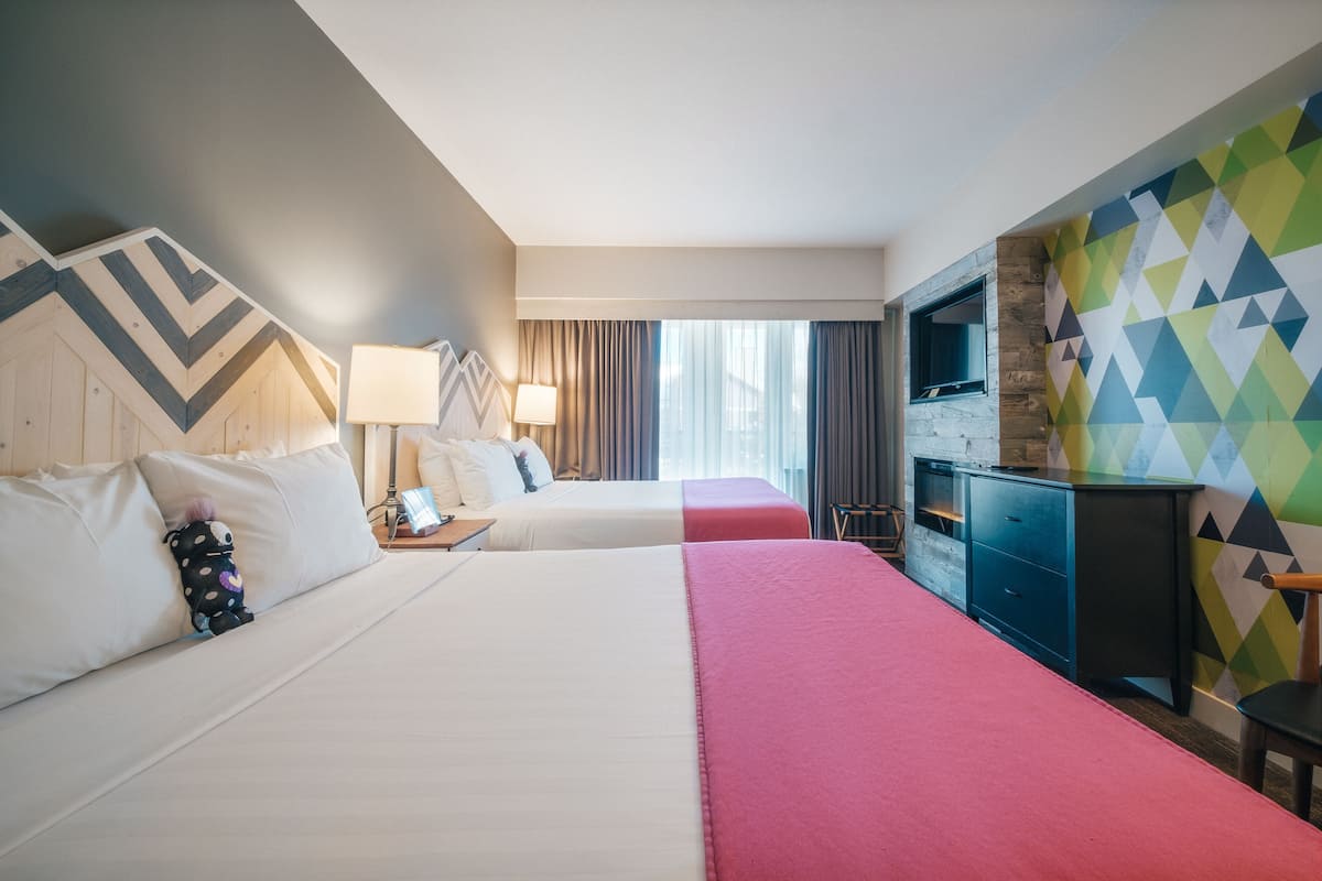 Een hotelkamer met twee bedden, een televisie, een bureau en een kleurrijke geometrische wand.