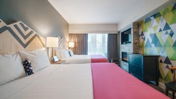 Habitación de hotel con dos camas, televisión, escritorio y pared con diseño geométrico colorido.
