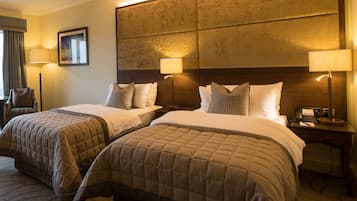 Habitación de hotel con dos camas tamaño queen, un gran cabecero acolchado, lámparas de noche, un escritorio con teléfono y una silla.