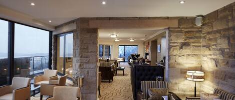 A spacious lounge area with a stone accent wall, comfortable seating, and a view of the outdoors.