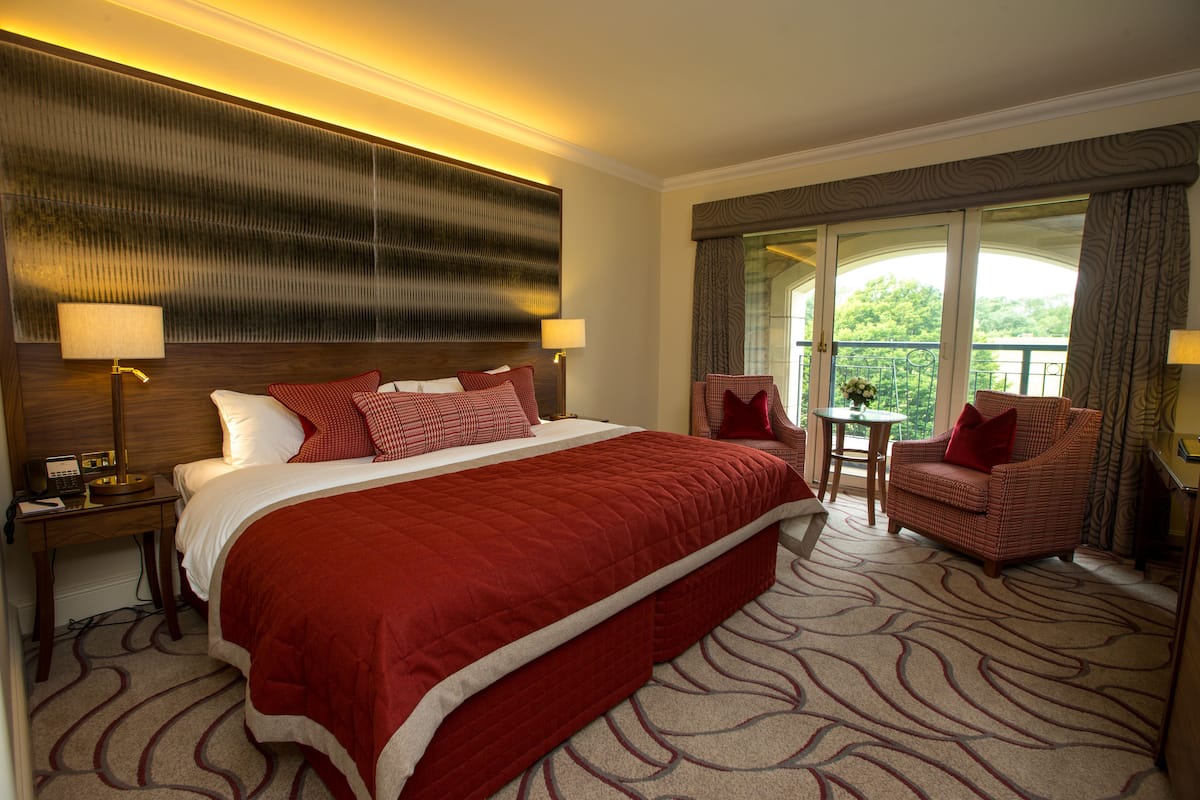 A hotel room with a large bed, a chair, a small table, and a balcony with a view.