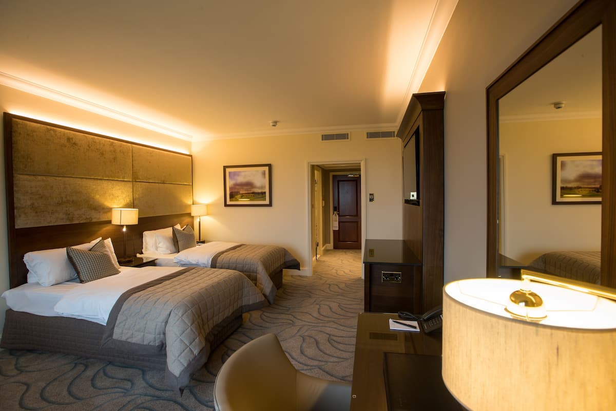 A hotel room with two beds, a desk, a chair, a large mirror, and a lamp.