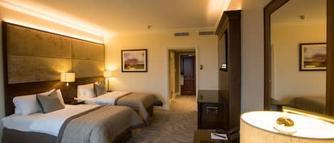 A hotel room with two beds, a desk, a chair, a large mirror, and a lamp.