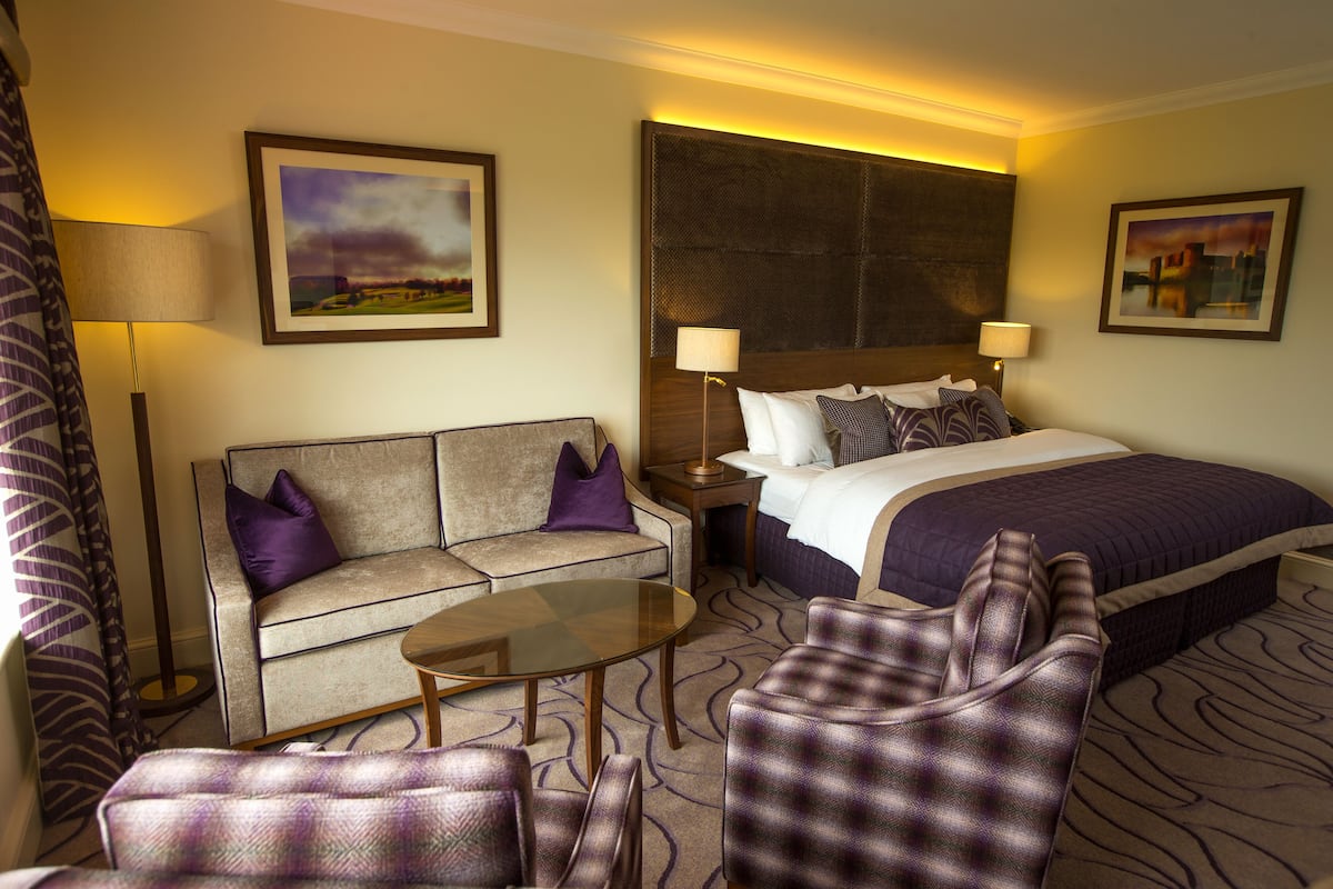 A hotel room with a bed, a sofa, a coffee table, and two armchairs.