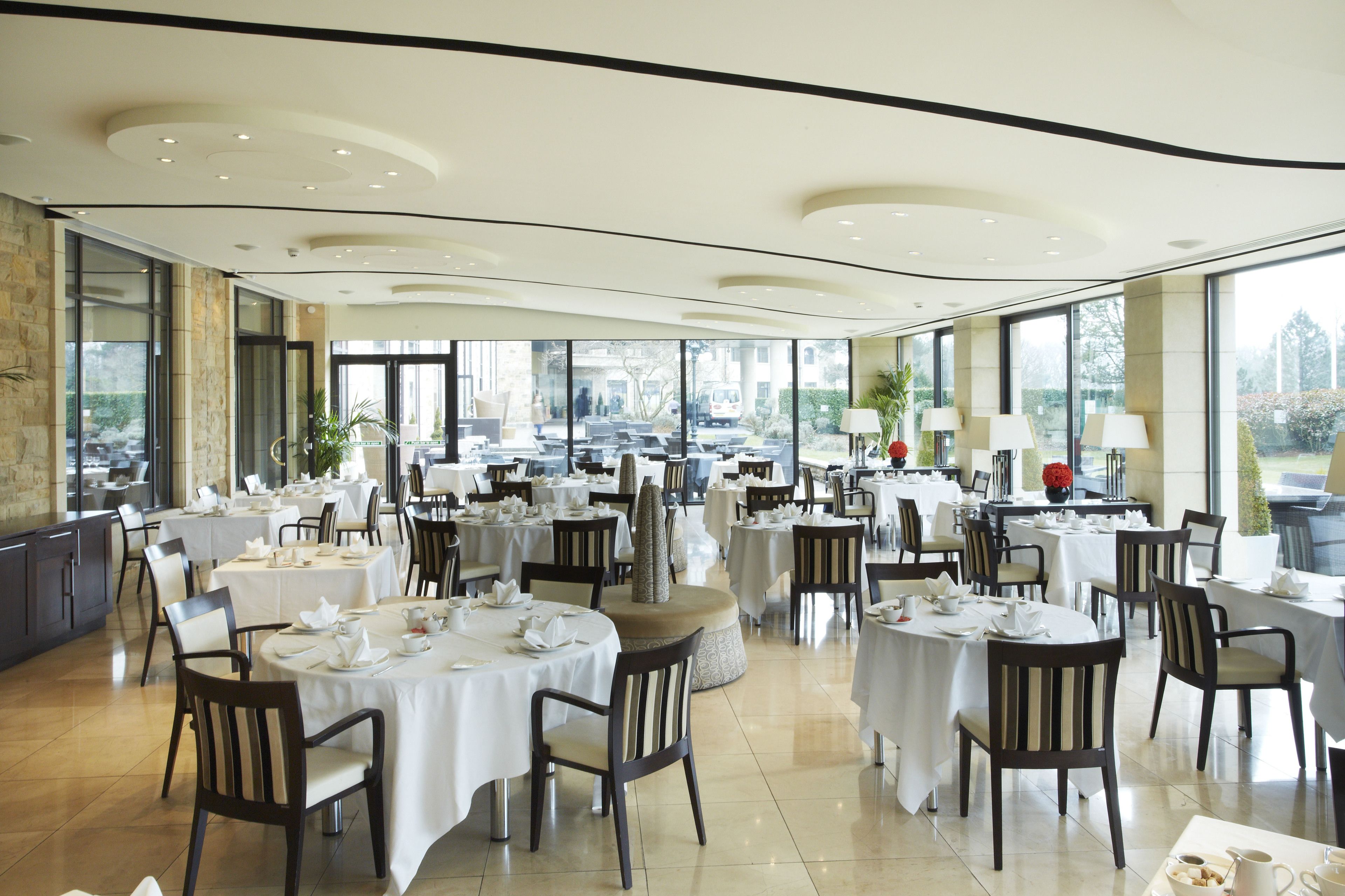 A spacious dining area with multiple round tables, chairs, and a modern ceiling design.